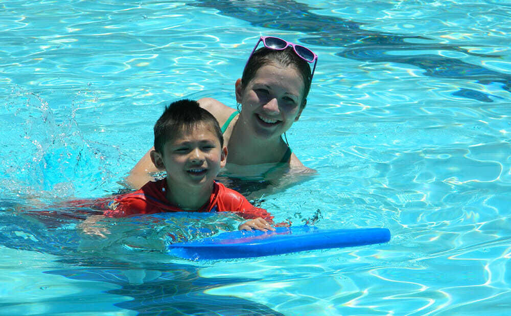 Counselor Guides Young Camper Doing Flutter Kicks at Swimming