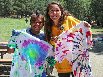 Camper and Counselor Smile While Holding Freshly Tie-Dyed Shirts