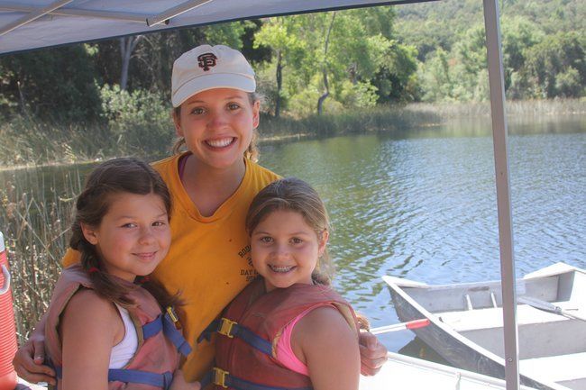 campers and counselor similing and hugging at waterfront at lafayette reservoir with boats